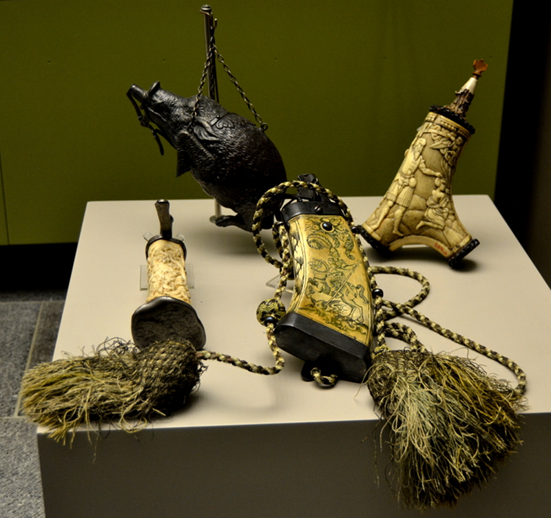 A collection of ornate powder horns. The one on the left is German dates to around 1600. It shows St. George and the dragon. The one in the back in the shape of a wild boar was made in Nuremberg in the first half of the 18th century. The other two are also German, from the end of the 18th century.