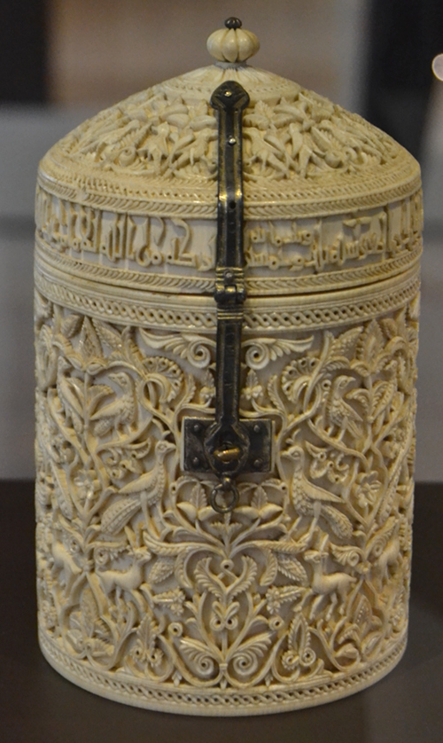 The Zamora pyxis, an ivory box with a dome-shaped lid that opens and closes with a hinge and a silver clasp with niello detailing. The delicate carving includes arabesques, palmettes, gazelles, peacocks, and other birds that recreate a palace garden. An Arabic inscription in Kufic-style calligraphy on the base of the lid indicates the date of manufacture (353 after Hijra / 964 AD), the artist (Durri al-Salir), the person who commissioned it (Caliph Al-Hakam II) and the recipient (the caliph’s favorite, Subh).