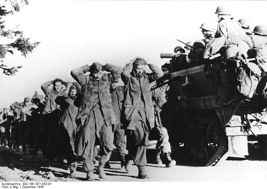 Nazi prisoners march to rear as Americans move forward. Private Frank Kolly (center), military policman of the Third U.S. Army's Fourth Armored Division, leads a group of Nazi prisoners to the rear as an American half-track rolls forward towards Bastegno, Belgium. Lieutenant General George S. Patton's men stabbed north from the Saar front to relieve on December 27, 1944, the U.S. forces which held out at Bastegno for nine days against all German attacks. By December 31, the German counter-thrust into Luxembourg and Belgium had cost the enemy more than 15,000 men taken prisoner by U.S. forces. U.S. Signal Corps Photo ETO-HQ-44-31309. Serviced by London OWI to list B-1 certified as passed by shaef censor