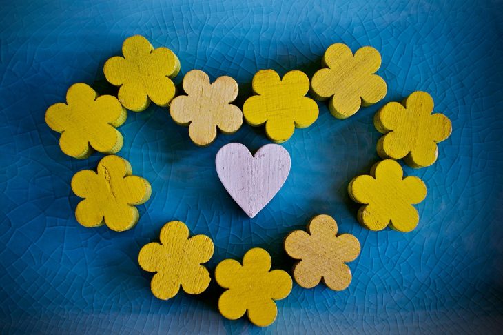 Yellow flowers make the shape of a love heart, centred on a pale pink love heart on a blue background.